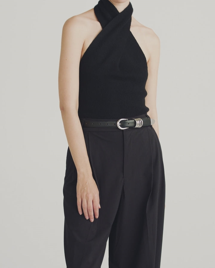 Model wearing Déhanche Hollyhock belt in sleek black leather with an intricate silver buckle, paired with a black sweater and high-waisted trousers, showcasing modern elegance and sophistication.