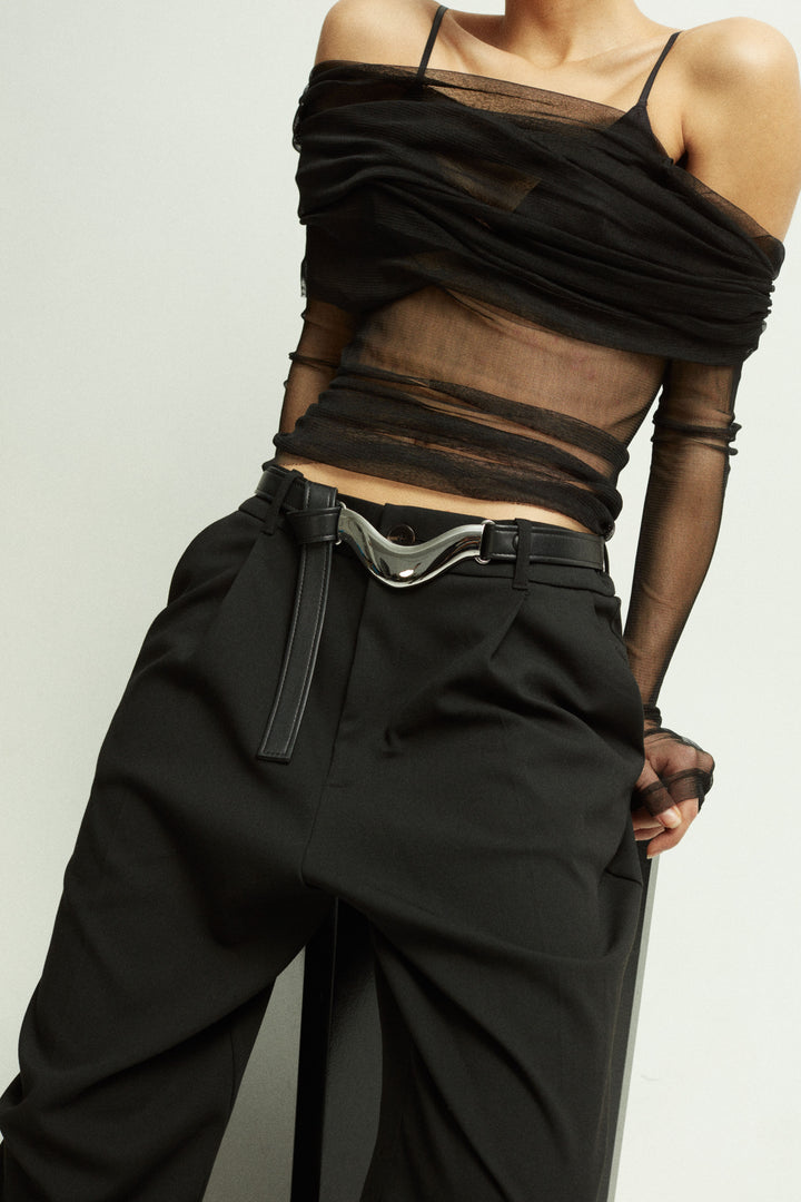 Model wearing Déhanche Brancusi belt in sleek black leather with a sculptural silver centerpiece, paired with a sheer black top and high-waisted pants, exuding modern sophistication.