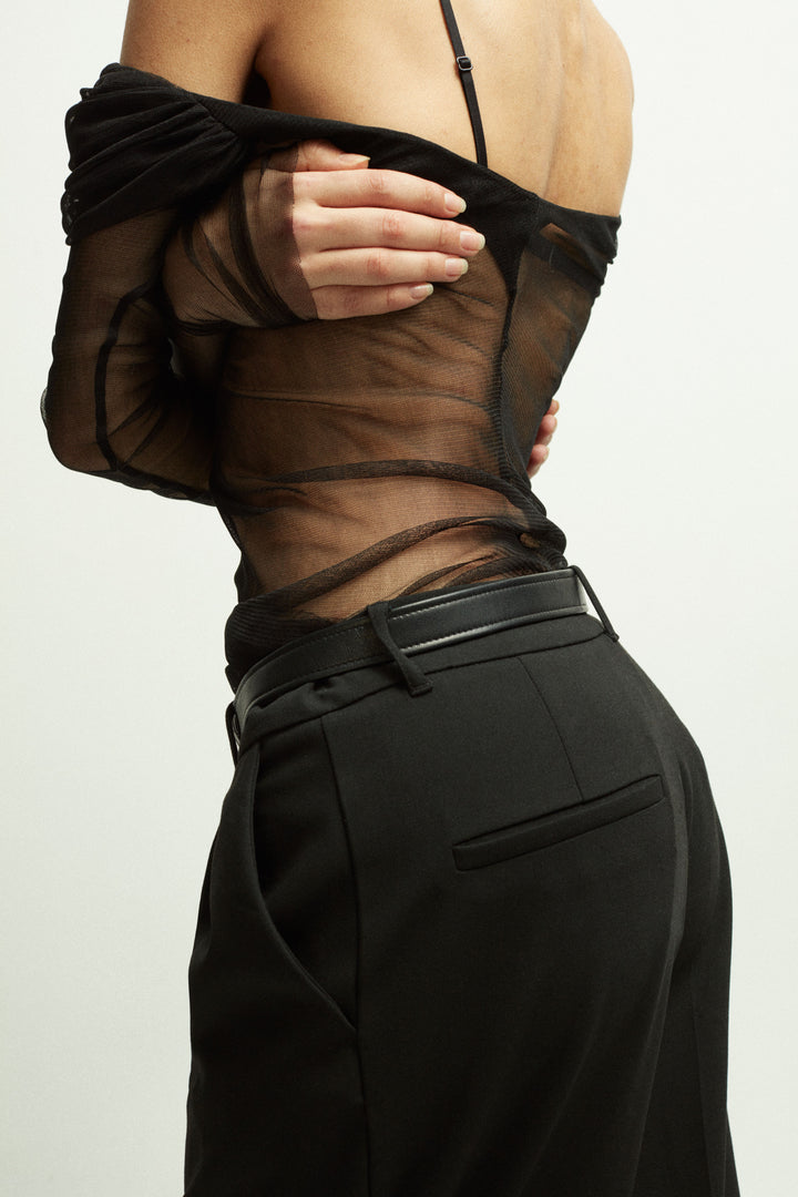 Model wearing Déhanche Brancusi belt in sleek black leather with a sculptural silver centerpiece, paired with a sheer black top and high-waisted pants, exuding modern sophistication.